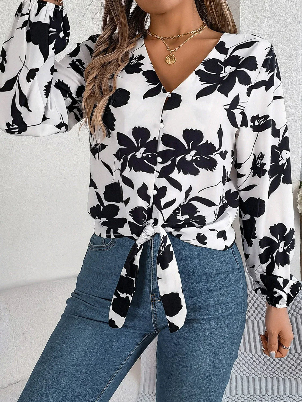 Woman wearing a white long-sleeve blouse with a black floral print and a tie-front detail, adjusting her sleeve.
