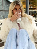 Woman wearing a white shaggy faux fur cropped jacket and light blue jeans, holding a coffee cup.