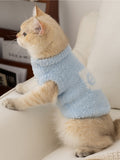 Side view of a cat wearing a light blue fluffy knit pet vest with a mock neck and a white graphic detail on the side.