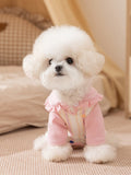 White dog wearing a pink and striped pet jumpsuit with a ruffled collar.