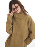 Woman in a camel oversized knit sweater with a button-up collar, smiling and adjusting the collar.