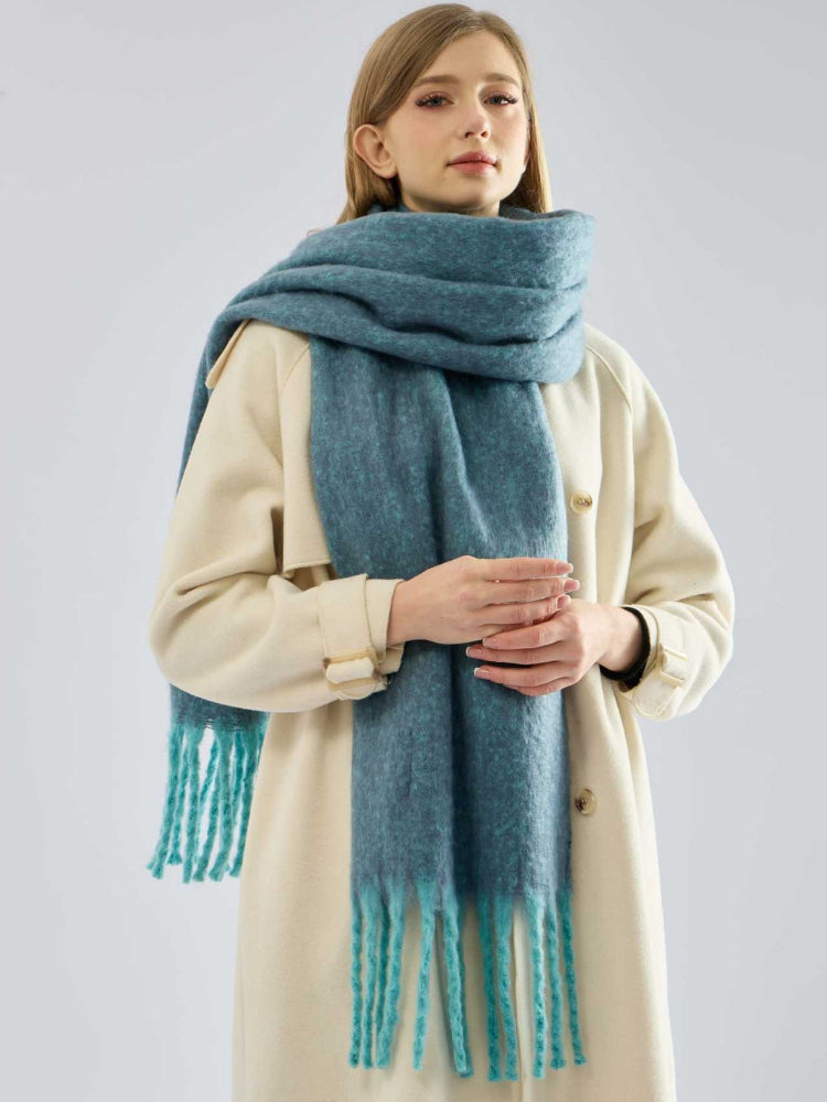 Woman wearing a teal oversized scarf with fringe detail over a cream coat.