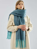 Woman wearing a teal oversized scarf with fringe detail over a cream coat.