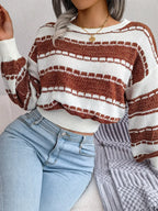Close-up of a woman wearing a white and brown striped knit sweater with a crew neck and long sleeves, and light wash denim jeans.