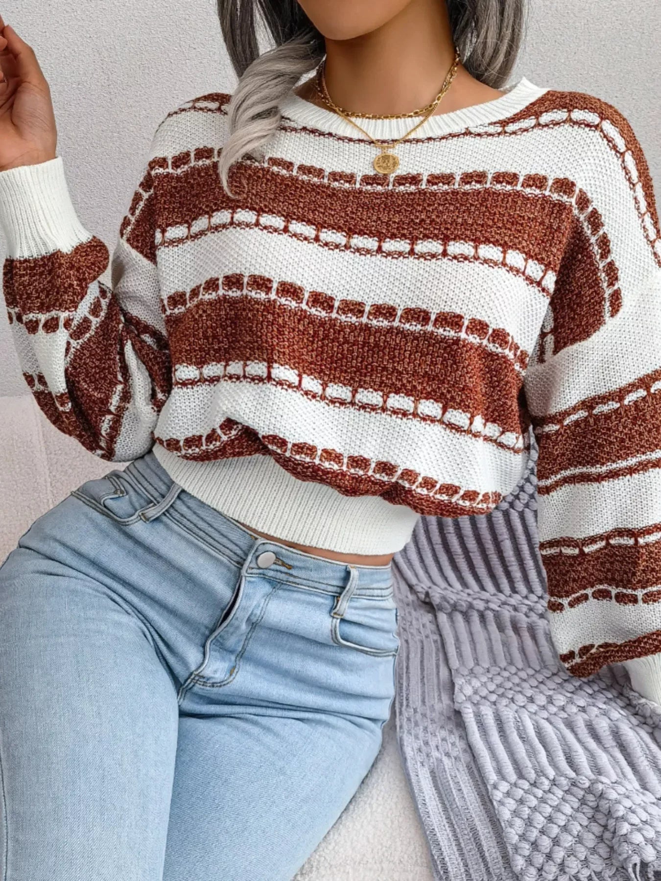 Close-up of a woman wearing a white and brown striped knit sweater with a crew neck and long sleeves, and light wash denim jeans.