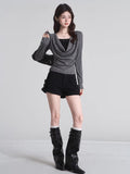 Full body shot of woman in grey draped cowl neck long sleeve top, black shorts, and black boots