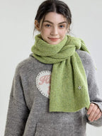 Woman modeling a light green ribbed knit scarf.