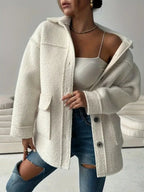 Front view of a woman in a cream-colored oversized fleece jacket, worn open over a white crop top and blue jeans.