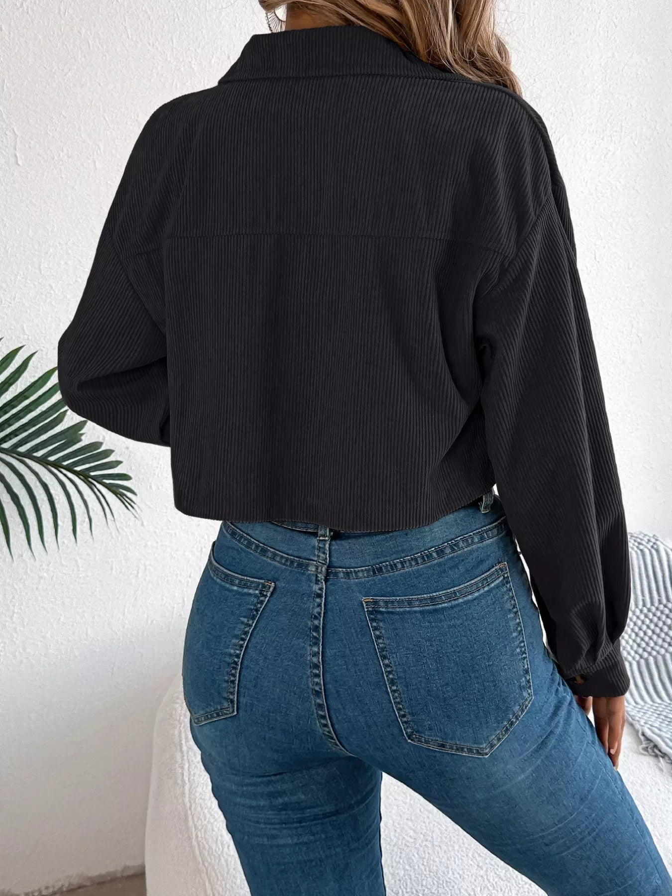 Back view of a woman in a black cropped corduroy jacket and blue jeans