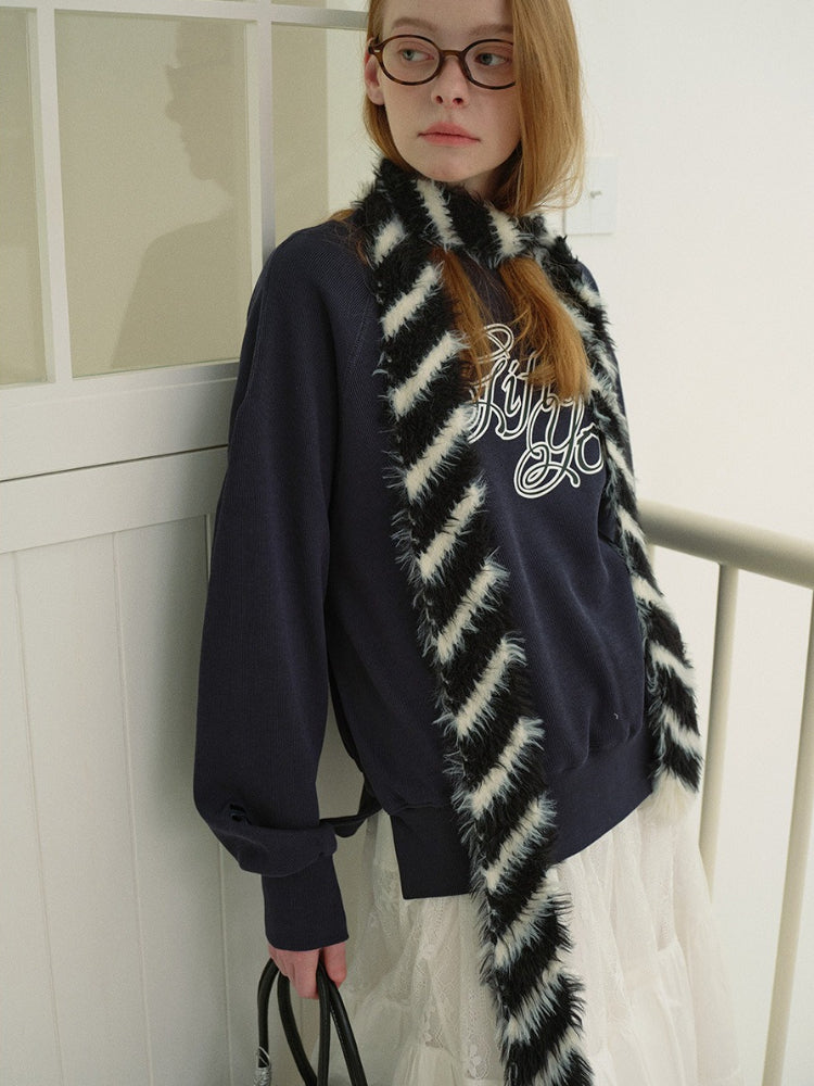 Model wearing a navy graphic print sweatshirt with a black and white striped faux fur scarf and a white tiered lace skirt.