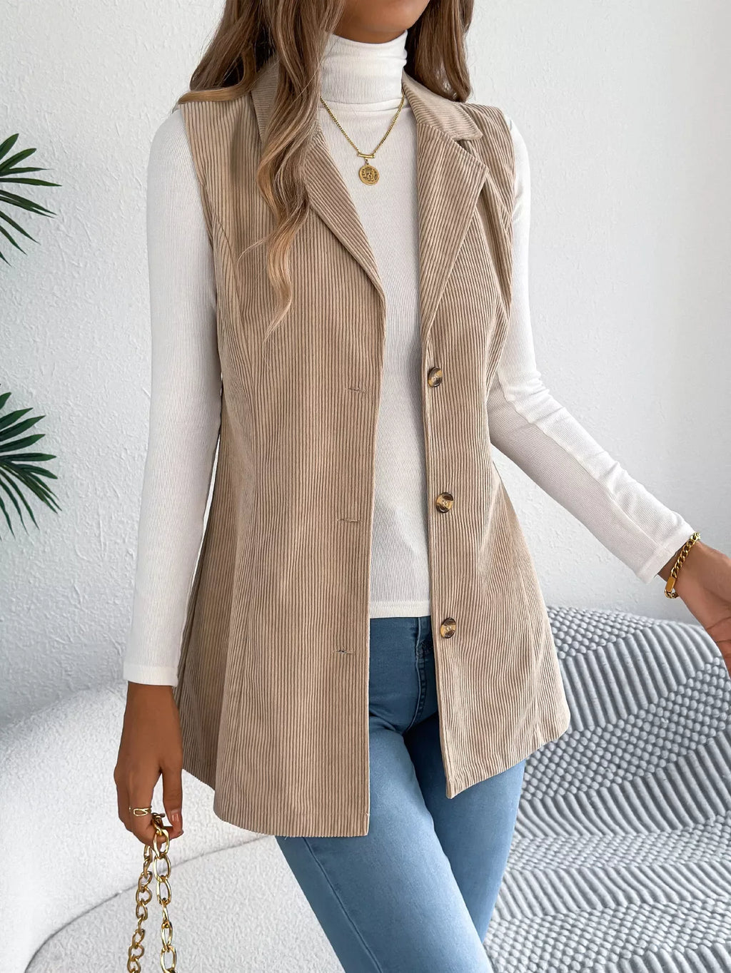 Front detail of a beige corduroy longline vest with notched lapels and button closure.