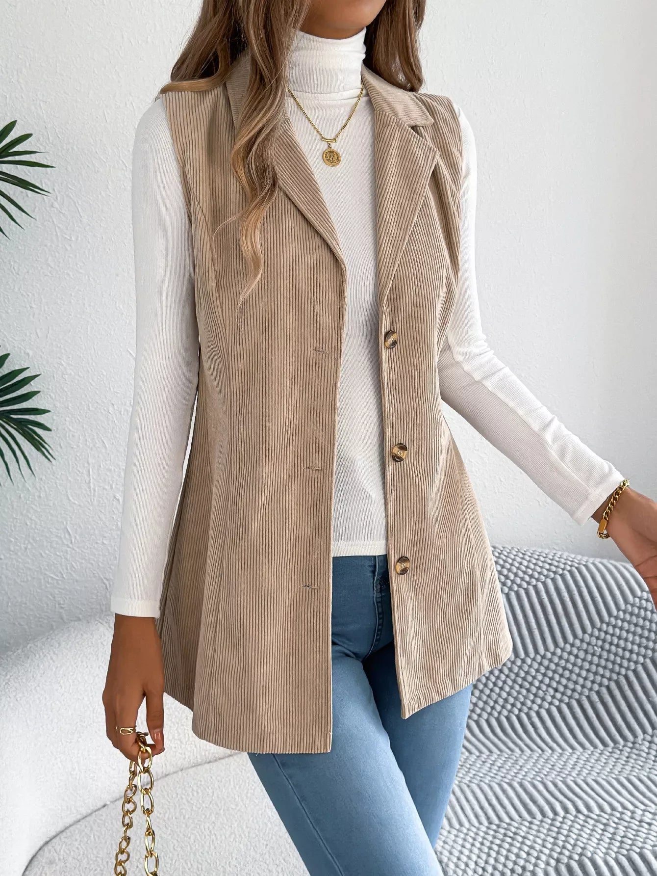Front detail of a beige corduroy longline vest with notched lapels and button closure.