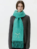 Woman wearing a teal scarf with a white bow embellishment and fringe, facing forward.