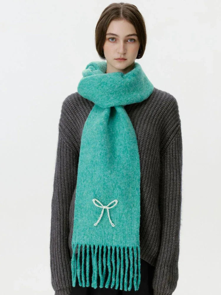 Woman wearing a teal scarf with a white bow embellishment and fringe, facing forward.