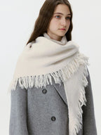 Woman wearing a cream-colored knit scarf with fringe detail over a grey coat.