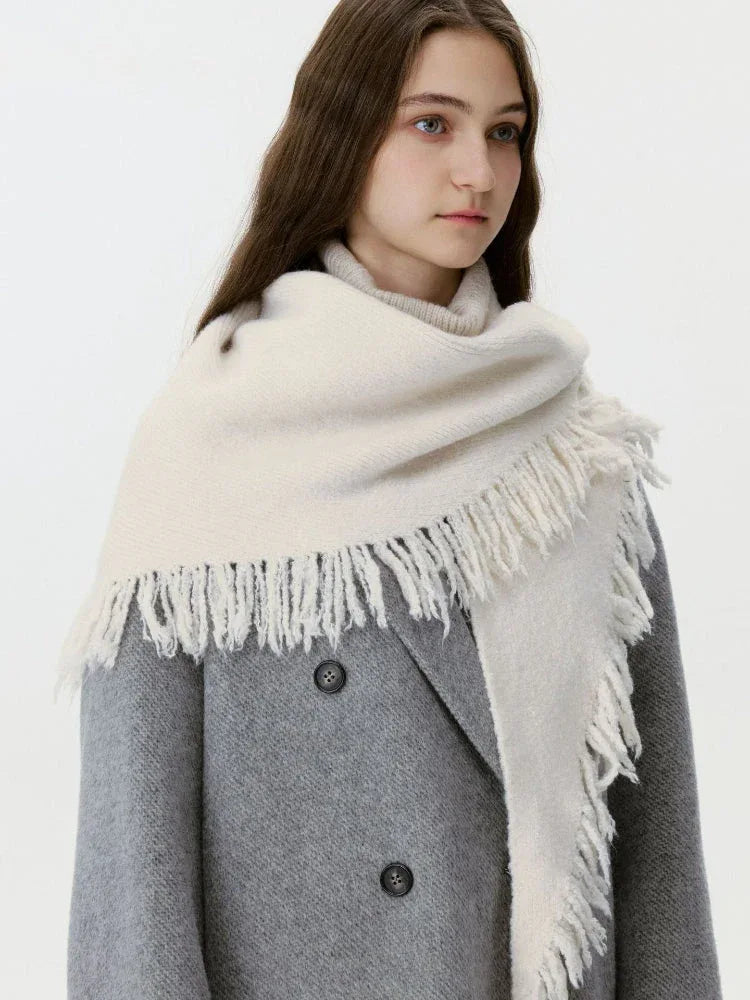 Woman wearing a cream-colored knit scarf with fringe detail over a grey coat.