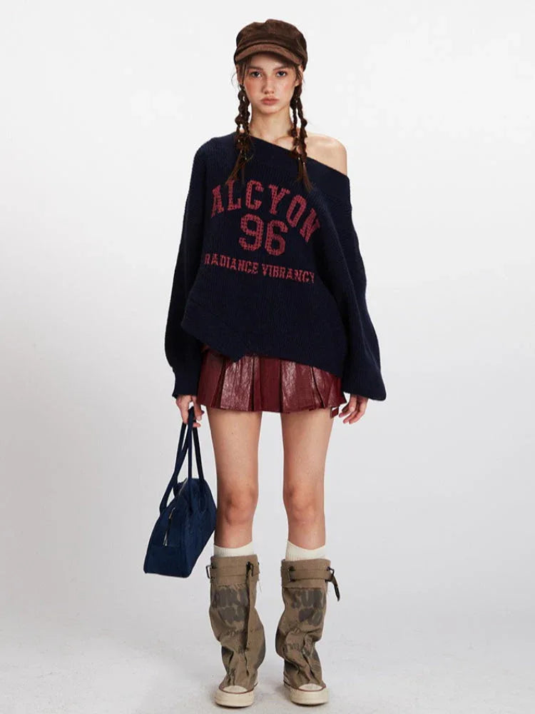 Woman wearing a navy blue oversized knit sweater with 'ALCYON 96 RADIANCE VIBRANCY' graphic print in red, paired with a burgundy faux leather pleated mini skirt and brown cap.