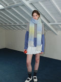 Full body shot of a woman wearing a long, ombre gradient scarf in yellow, blue, and green, draped loosely around her neck.