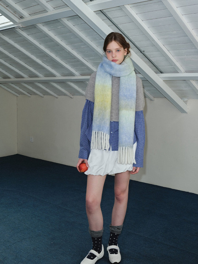 Full body shot of a woman wearing a long, ombre gradient scarf in yellow, blue, and green, draped loosely around her neck.