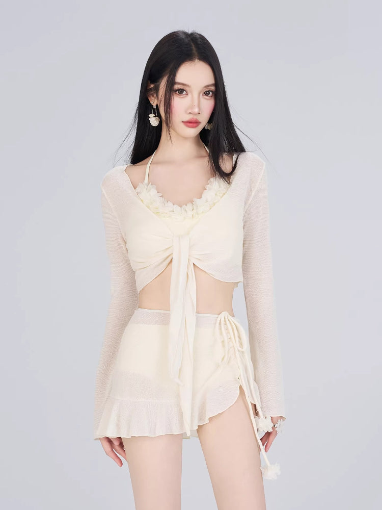 Woman wearing a cream-colored sheer long sleeve tie-front cover-up over a matching bikini top and shorts.