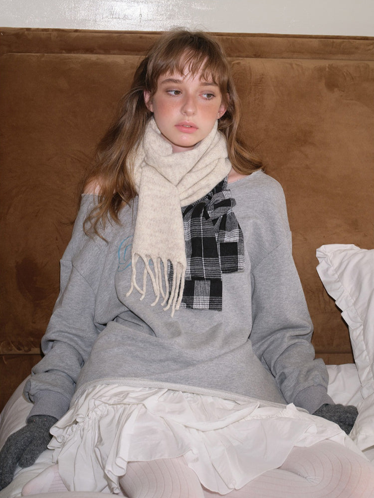 Woman sitting on a bed wearing a grey sweatshirt and cream scarf