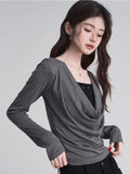 Close-up of a woman's upper body wearing a grey long-sleeve draped cowl neck top and a black camisole.