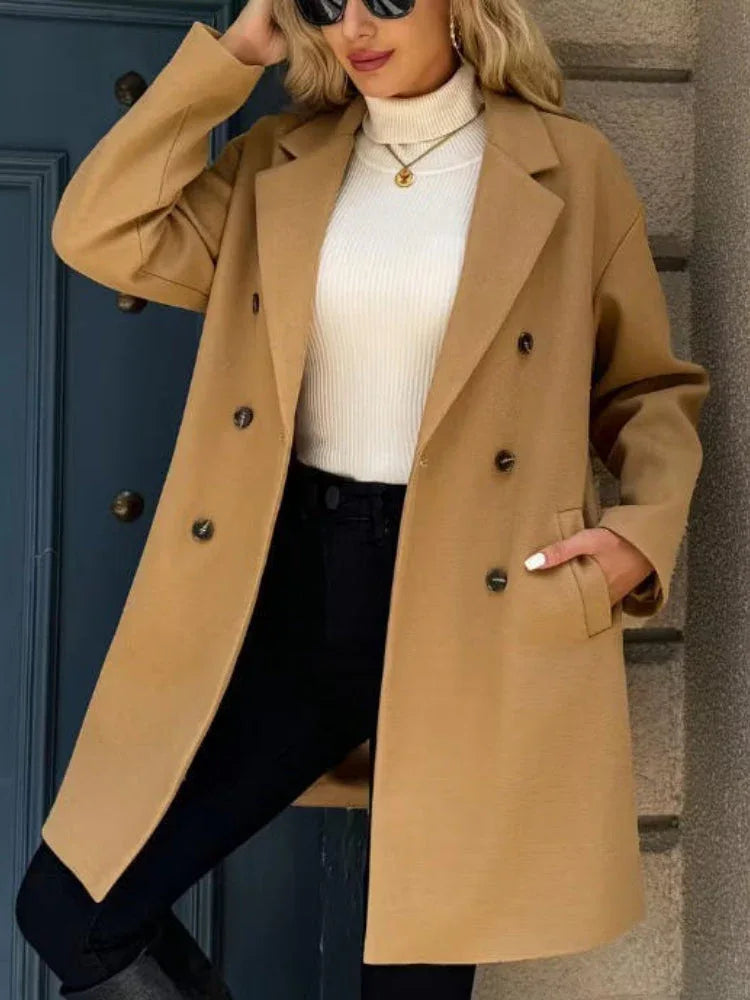 Woman wearing a camel double-breasted wool blend coat with a notched lapel collar, paired with a white turtleneck and black pants. Main image