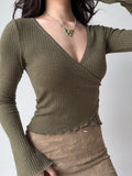 Woman in a green ribbed wrap top and a beige patterned skirt, accessorized with a butterfly necklace.