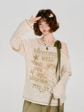 Woman wearing a cream-colored long-sleeved graphic t-shirt with distressing and an off-the-shoulder detail.