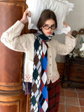 Woman wearing a cream cable knit cardigan, plaid skirt, and argyle scarf