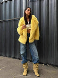 Woman in a yellow faux fur jacket, white crop top, and blue jeans