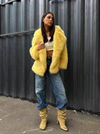 Woman in a yellow faux fur jacket, white crop top, and blue jeans