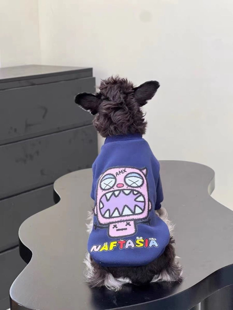 Miniature schnauzer puppy wearing a navy blue dog sweatshirt with a pink monster graphic on the front and a silver chain collar.