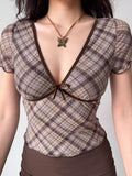 Detail shot of the neckline and bust of a brown plaid top featuring a V-neck and bow.