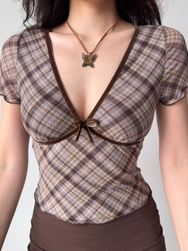 Detail shot of the neckline and bust of a brown plaid top featuring a V-neck and bow.