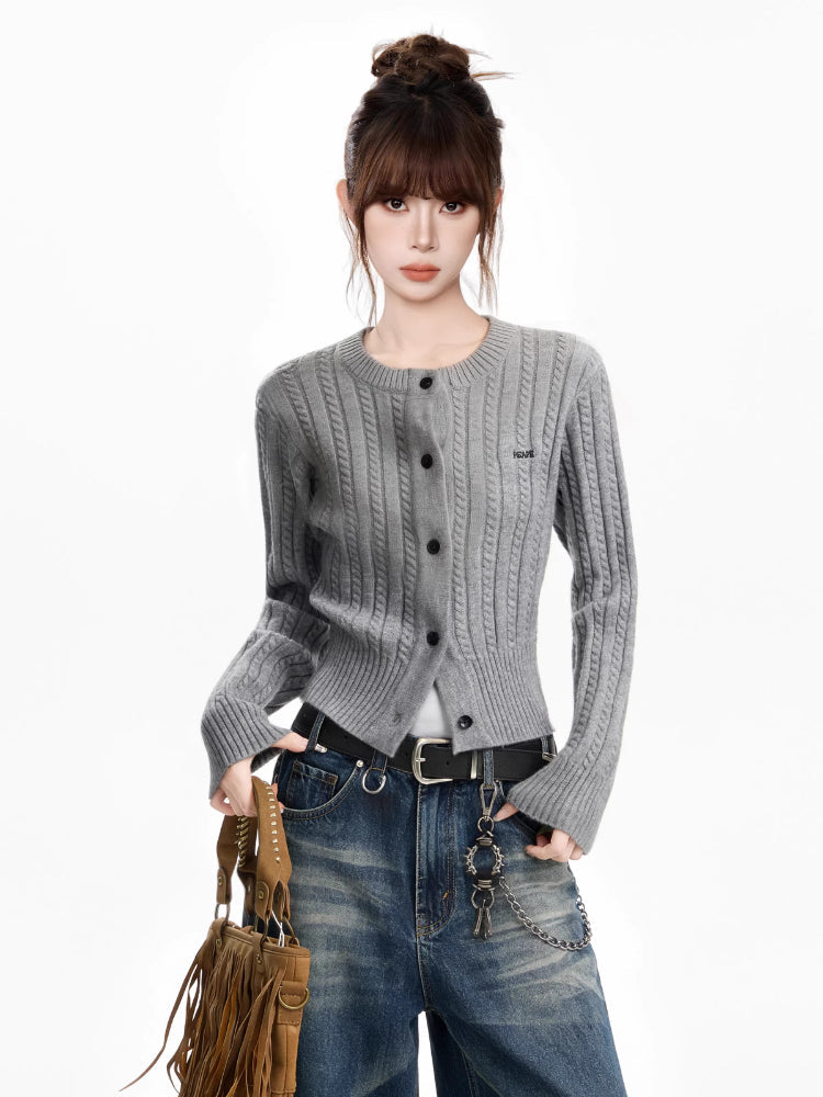 Woman wearing a grey cable knit cropped cardigan with a crew neck and button front, paired with blue wash jeans and a fringed handbag.