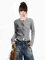 Woman wearing a grey cable knit cropped cardigan with a crew neck and button front, paired with blue wash jeans and a fringed handbag.