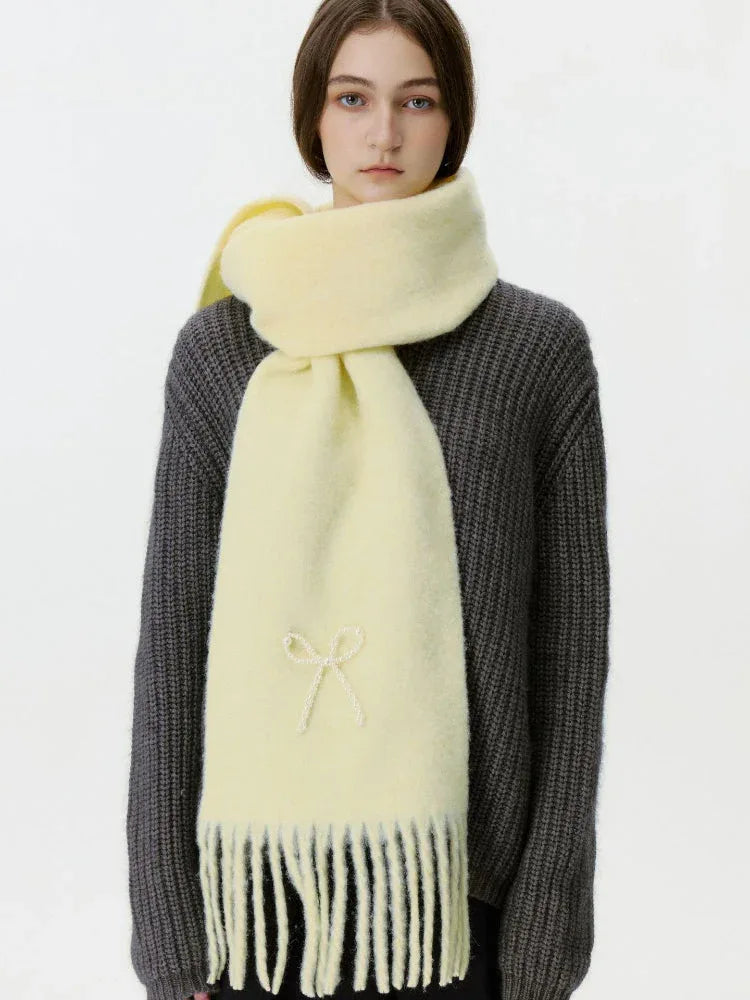 Woman wearing a light yellow scarf with a white bow embellishment and fringe.
