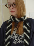 Full body shot of a model in a navy graphic print sweatshirt, white tiered lace skirt, and brown boots, accessorized with a striped faux fur scarf and a black handbag.