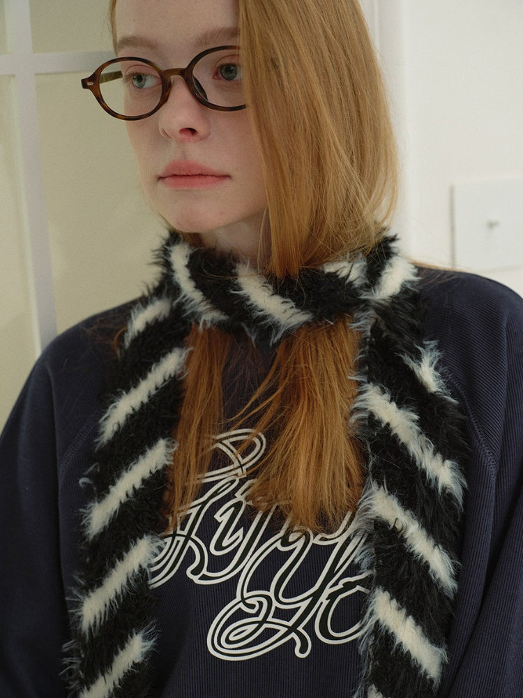Full body shot of a model in a navy graphic print sweatshirt, white tiered lace skirt, and brown boots, accessorized with a striped faux fur scarf and a black handbag.