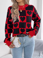 Woman wearing a red and black checkerboard knit sweater with black heart patterns, light wash denim jeans, a black belt, and a white quilted handbag with a gold chain strap.