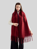 Full body shot of a woman wearing a burgundy knit scarf with fringed ends and blue contrast stitching.