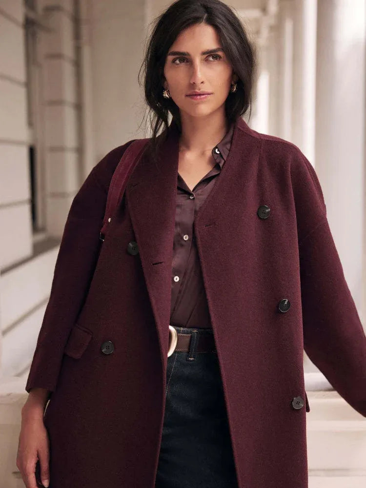 Woman wearing a burgundy double-breasted wool blend coat with dark wash jeans and a brown belt