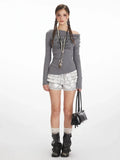 Woman wearing a grey long-sleeve off-the-shoulder top with graphic print and layered ruffled silver shorts.