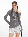 Front view of a woman wearing a grey long-sleeve off-the-shoulder top with graphic print and layered ruffled silver shorts, with braids.
