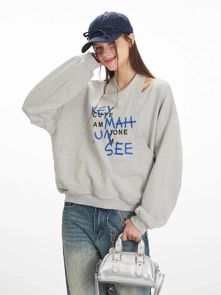Close-up of a woman wearing a grey graphic print sweatshirt with a cut-out neckline and blue text, posing with her hand on her head.
