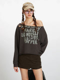 Close-up front view of a woman wearing a dark grey distressed graphic print cropped sweatshirt with an off-the-shoulder neckline, showing graphic print detail.