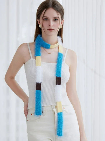 Woman wearing a white ribbed tank top and cream pants, accessorized with a long, fuzzy knit scarf featuring alternating blocks of blue, yellow, white, and brown.