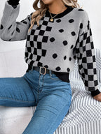 Woman sitting on a couch wearing a grey knit sweater with black checkerboard and polka dot patterns, and blue jeans.