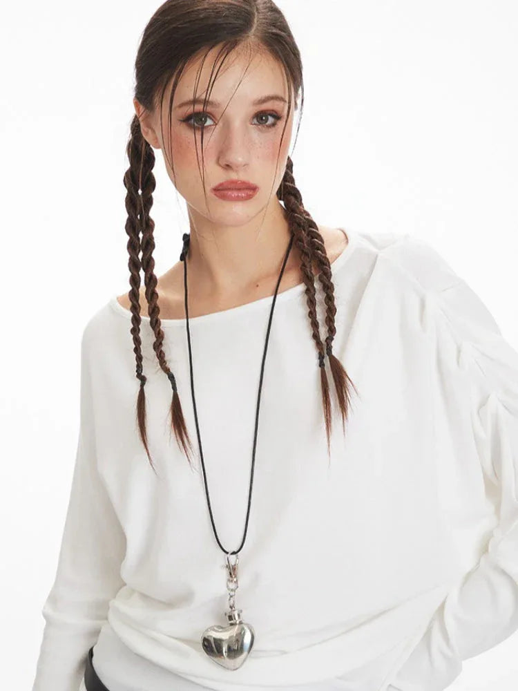 Front view of a model's upper body, highlighting the white long-sleeve top and necklace.